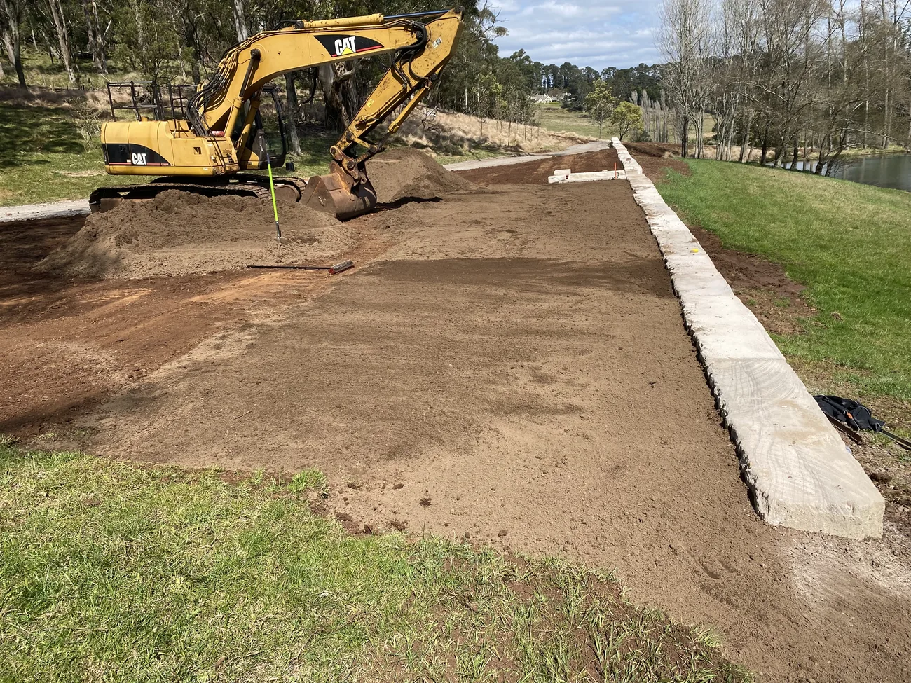 Excavator grading an access strip beside a sandstone block wall