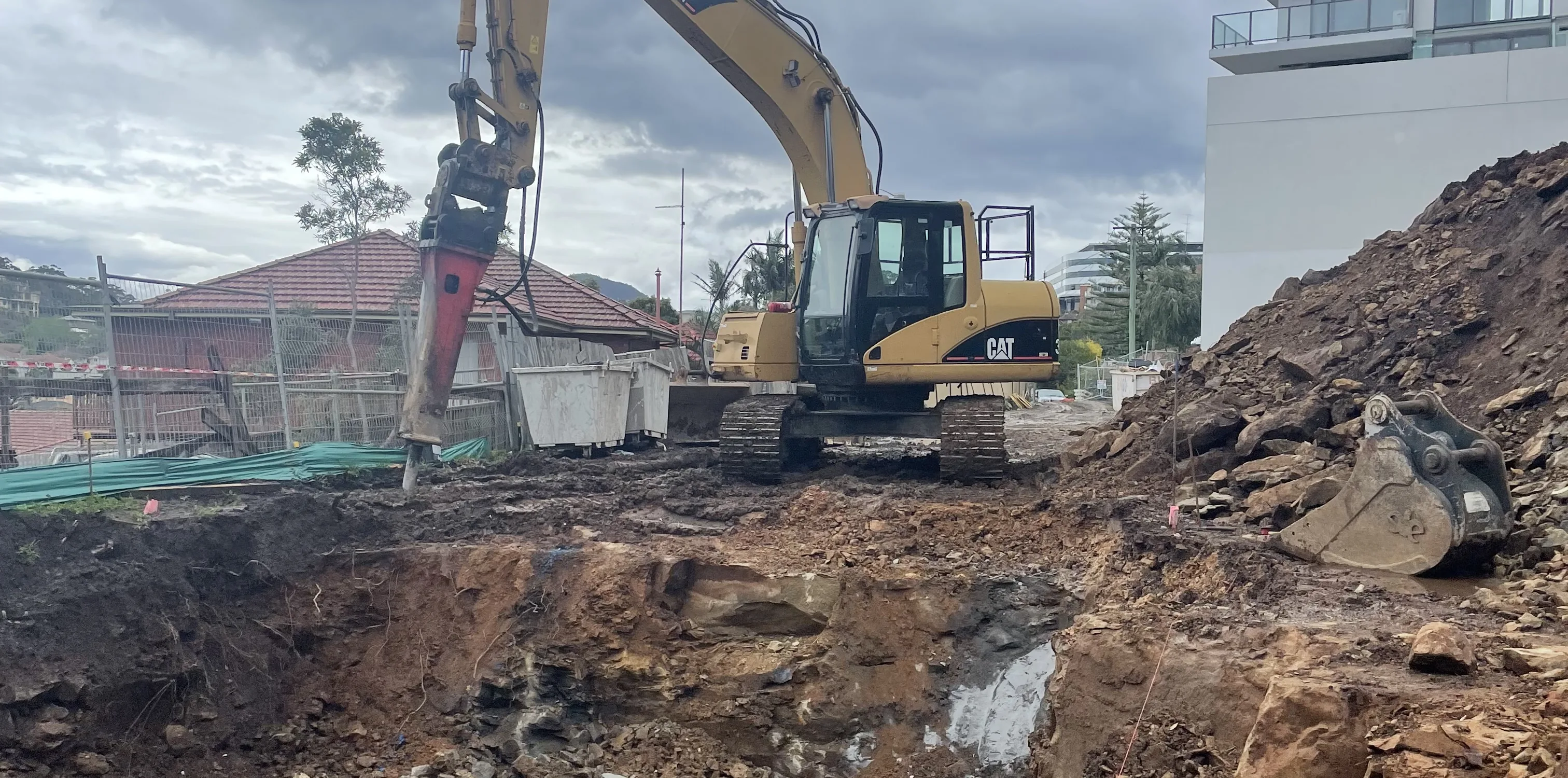 Excavator and rock breaker working a tight block beside housing