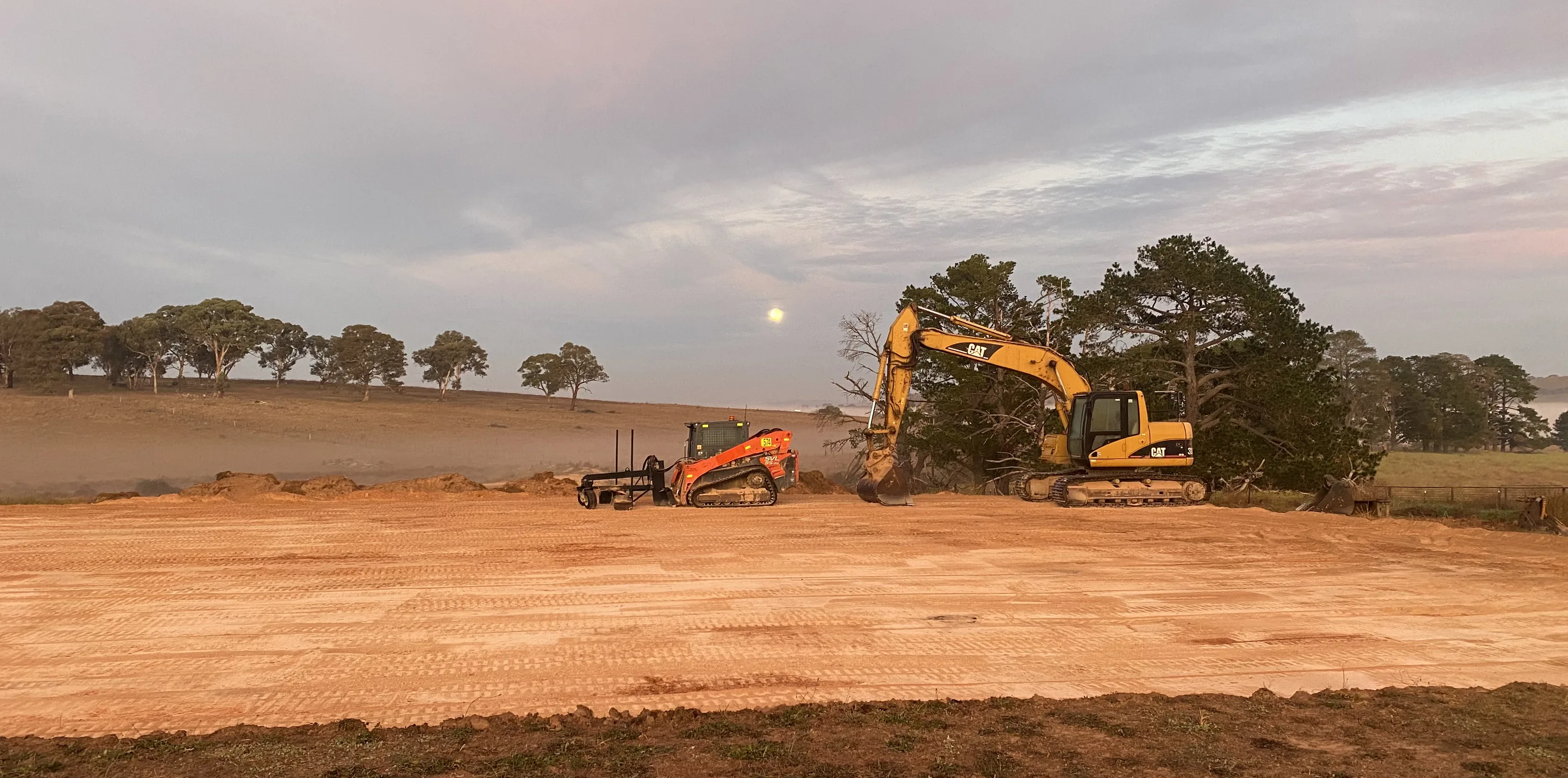 Two Alliance Excavations machines grading open ground at dusk